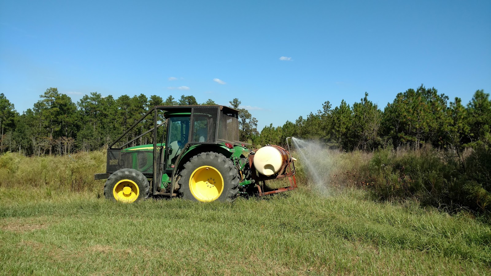 farm tractor with a metal cage and spray tank being used to spray herbicides